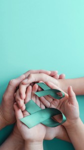 Adult and children hands holding Teal ribbons on blue background, Ovarian Cancer, cervical Cancer, anti bullying and sexual assault awareness